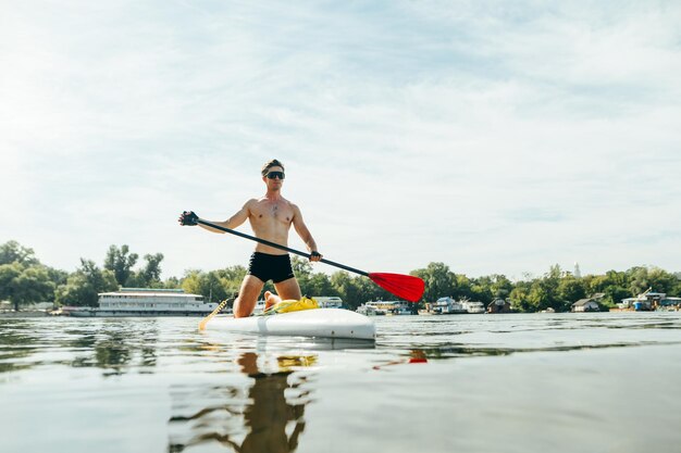 Atletische man zwemt op een vijver in de zomer op een zonnige dag op een sup board met een roeispaan in zijn handen