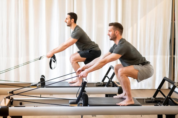 Atletische mannen doen squats op pilatesmachine