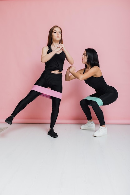 Atletische meisjes in zwarte sportkleding op een roze achtergrond doen squats van hoge kwaliteit foto