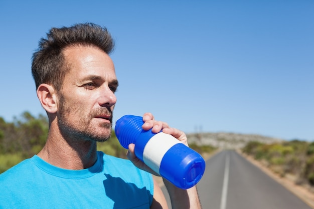 Atletische mens die op open weg een drank neemt