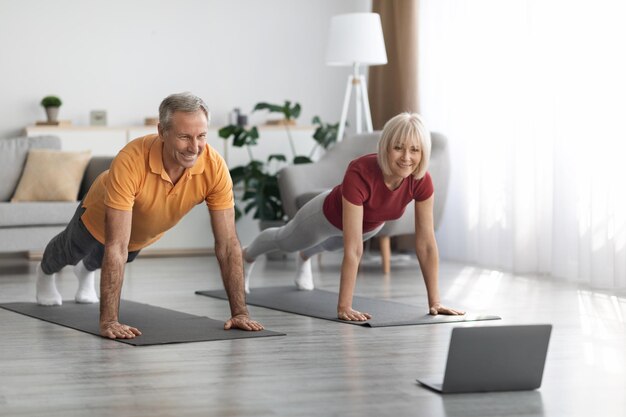 Atletische senior echtgenoten trainen thuis met behulp van notebook