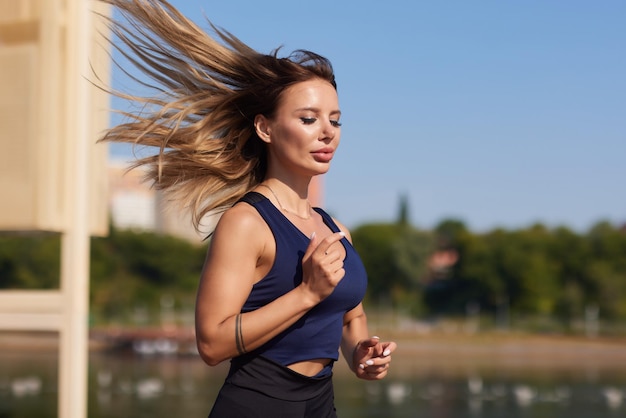 Atletische slanke vrouw op een zonnige dag loopt langs de dijk of het park