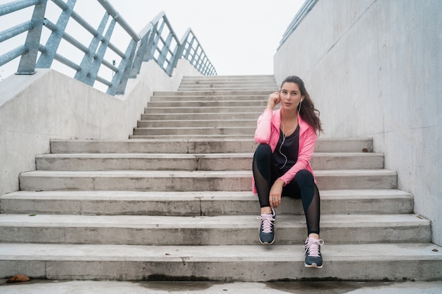 Atletische vrouw die aan muziek op een onderbreking van opleiding luistert.