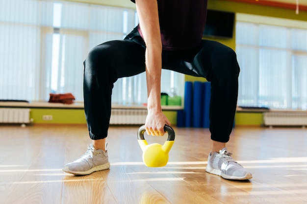 Atletische vrouw die met ketelklok uitoefenen terwijl het zijn in hurkende positie. spiervrouw die dwars geschikte training doen bij gymnastiek.