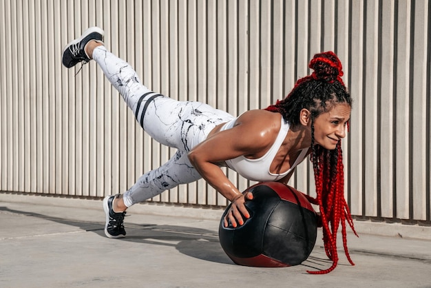 Atletische vrouw die oefening doet, heft benen op met med bal Kracht en motivatie Foto van sportieve vrouw in modieuze sportkleding