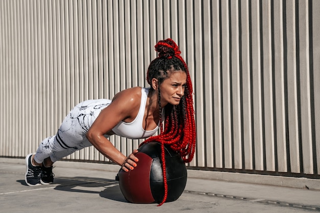 Atletische vrouw die oefeningsopdrukoefeningen met med bal doet. Kracht en motivatie. Foto van sportieve vrouw in modieuze sportkleding