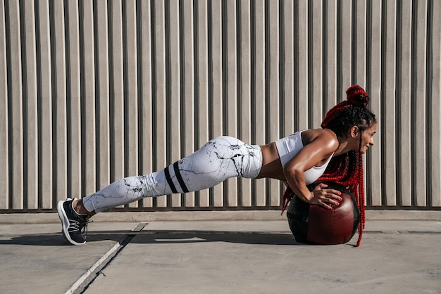 Atletische vrouw doet oefening push-ups met med bal Kracht en motivatie Foto van sportieve vrouw in modieuze sportkleding