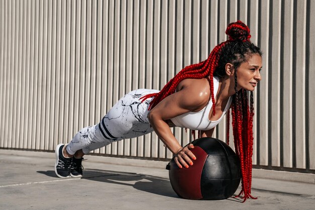 Atletische vrouw doet oefening push-ups met med bal Kracht en motivatie Foto van sportieve vrouw in modieuze sportkleding