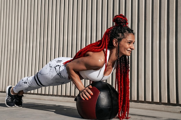 Atletische vrouw doet oefening push-ups met med bal Kracht en motivatie Foto van sportieve vrouw in modieuze sportkleding