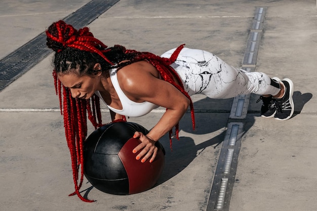 Atletische vrouw doet oefening push-ups met med bal Kracht en motivatie Foto van sportieve vrouw in modieuze sportkleding