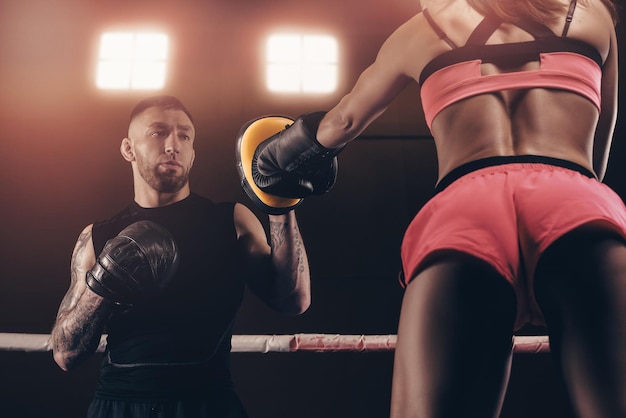 Atletische vrouw in rode korte broek en top is aan het boksen met een trainer Boksen en mixed martial arts concept