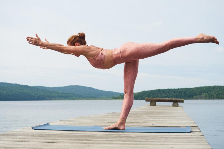 Atletische vrouw in roze sportkleding die een yoga-pose doet op een houten brug in de buurt van de zee
