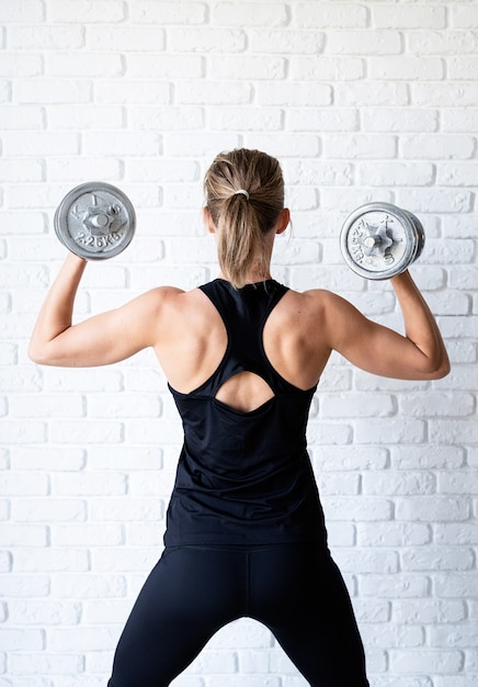 atletische vrouw in zwarte sportwear die haar rug en wapenspieren toont die met een halter trainen