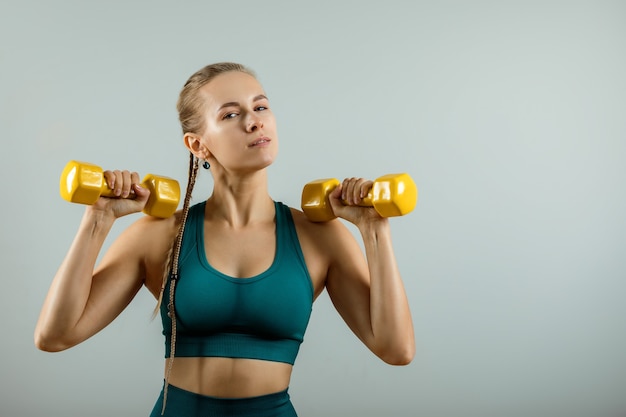 Atletische vrouw met halters in handen op een grijze achtergrond, fitness banner, fitness motivatie. foto van een gespierd fitnessmodel dat traint met halters op een grijze achtergrond.