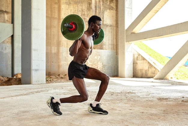 Atletische zwarte jongeman die een zwaargewicht halter optilt in een buitengymnastiek onder de brug Gezond levensstijlconcept
