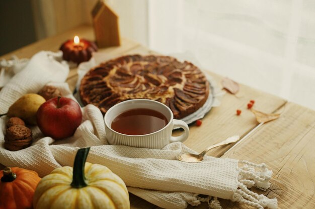 Photo atmospheric autumn still life warm tea in cup on wooden table with apple pie candle autumn leaves