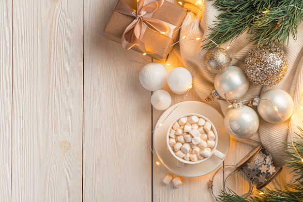 Atmospheric Christmas background with a cup of coffee and Christmas decorations on a light background in the light of burning lights. Top view, copy space.