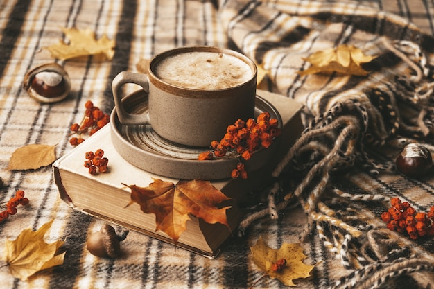 Atmospheric cozy autumn composition hot mug of coffee book fall leaves chestnut ashberry acorns and ...