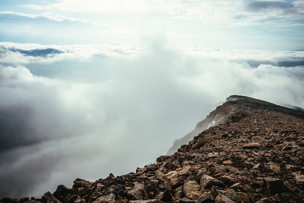 Atmospheric highlands scenery on top of mountain ridge above thick low clouds. Minimalist view from precipice edge over clouds. Beautiful minimal alpine landscape with mountain range over dense clouds