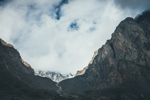 Paesaggio atmosferico con ruscello di montagna in una stretta valle tra alte montagne rocciose. nuvole basse sulla montagna con neve. bella valle di montagna con torrente di montagna. splendida valle tra rocce taglienti.