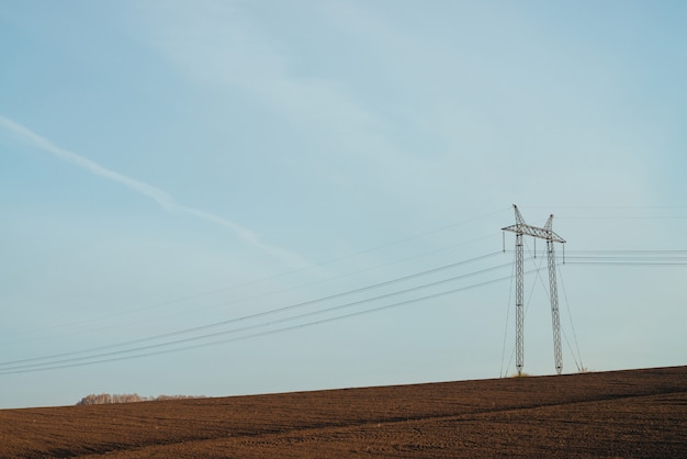 Atmospheric landscape with power lines in field under blue sky. 