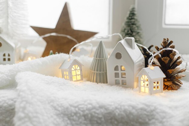 雰囲気のあるミニチュア冬の村スタイリッシュなかわいい小さなセラミックの家と輝くライトと柔らかい雪の毛布の上のクリスマスの木の木クリスマス モダンな白い背景ハッピー ホリデー