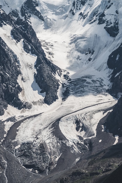 Paesaggio alpino strutturato minimalista atmosferico della montagna rocciosa innevata con la lingua del ghiacciaio.