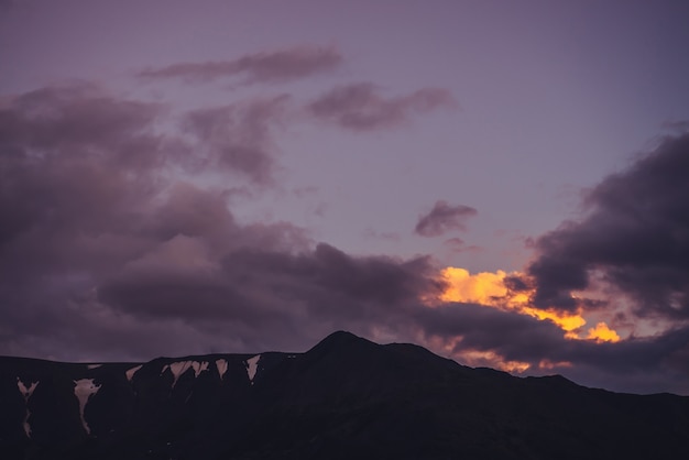 Atmosferico scenario di montagna con cielo lilla all'alba. paesaggio panoramico con rocce con neve sotto il cielo al tramonto viola. bellissima alba in montagna in toni pastello. colore illuminante nel cielo nuvoloso dell'alba.