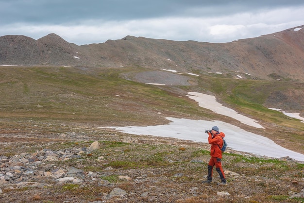 Atmospheric scenery with man in red against mountain range with sharp rocks under gray cloudy sky Tourist with camera shoots dramatic mountain landscape Man photographs mountains at gloomy weather