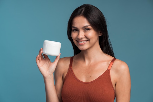 Attactive brunette lady with a bottle of cream smiling at camera