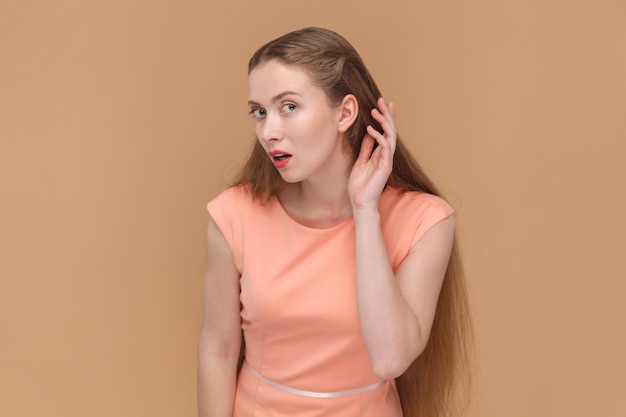 Фото Привлекательная милая женщина с длинными волосами, стоящая с рукой возле уха и слушающая чей-то шепот