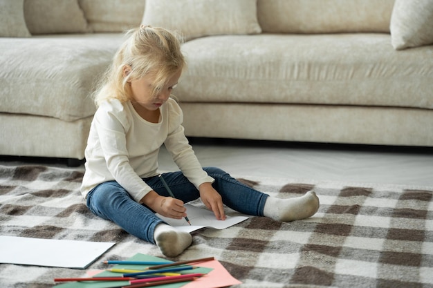 Attent meisje van voorschoolse leeftijd zittend op de vloer in een gezellig appartement maakt grappige foto's