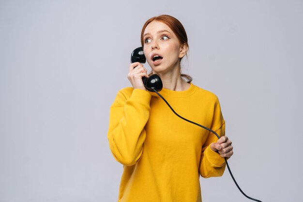 Attente jonge vrouw in stijlvolle gele trui praten over retro telefoon en wegkijken