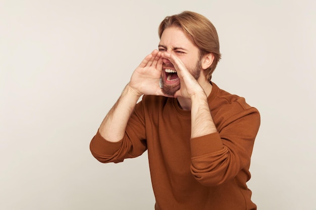 Attention, announcement. Portrait of annoyed aggressive man holding hands shaped as megaphone