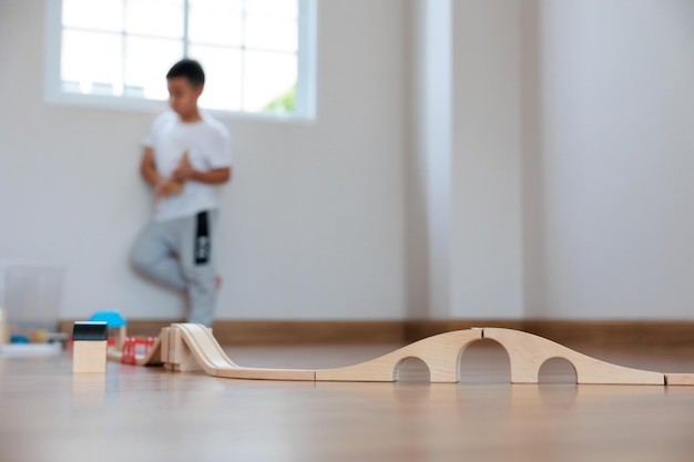 Внимание, азиатский мальчик, играющий в деревянный блок, строит железную дорогу и дорогу на полу дома Blackground