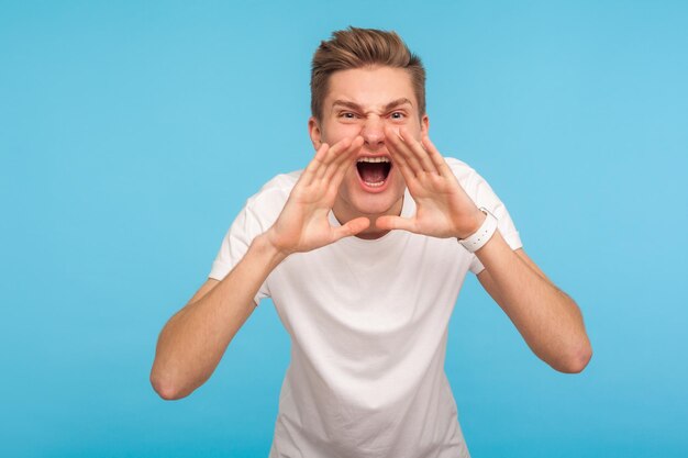 Attention Portrait of angry man in tshirt screaming loudly emotionally negative announcement shouting bad news with aggressive furious expression indoor studio shot isolated on blue background