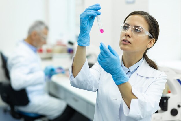 Foto operatore medico castana attento che controlla liquido rosa