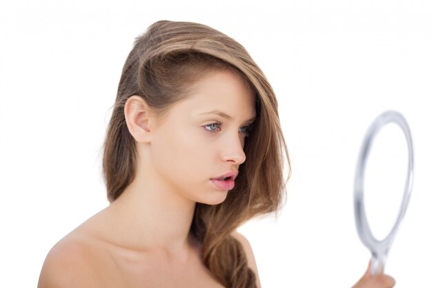 Attentive brunette model looking herself in a mirror