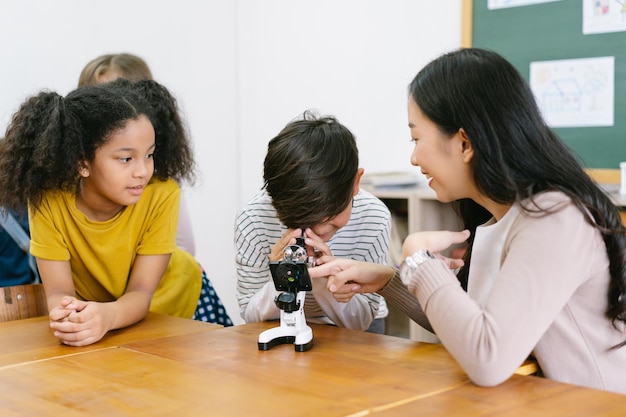 Photo attentive elementary schoolboy and asian female teacher with microscopes in science classroom at school with friends education elementary school learning science workshop conceptxa