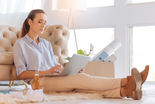 Attentive person. Responsible attentive enthusiastic woman sitting comfortably and typing a text while drinking alcohol at home