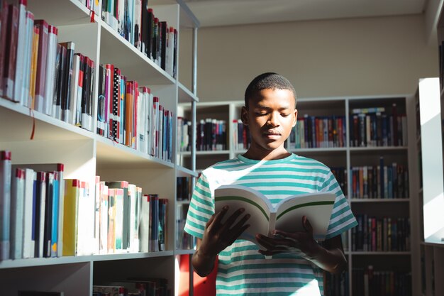 Attentive schoolboy reading book in library