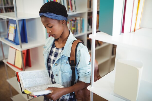 Внимательная школьница читает книгу в библиотеке