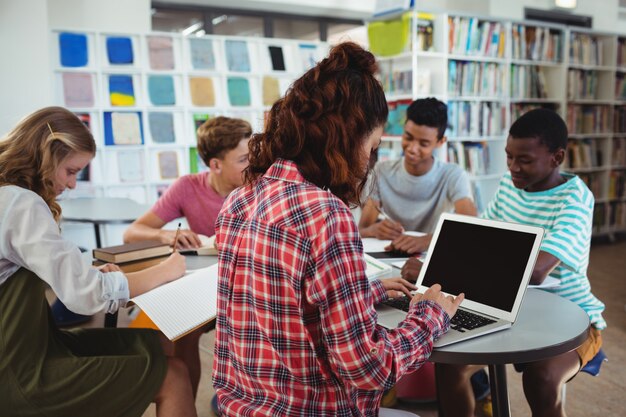 Attentive schoolgirl using laptop with her classmates