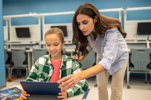 Photo attentive teacher touching tablet of girl sitting at desk