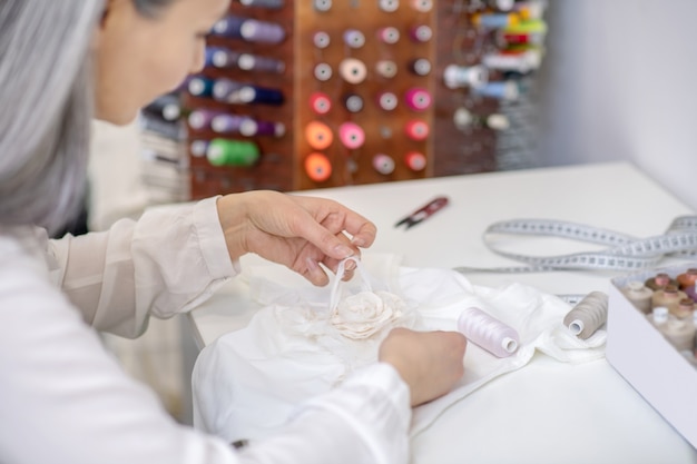 Attenta donna con lunghi capelli grigi che ripara i vestiti al tavolo in officina