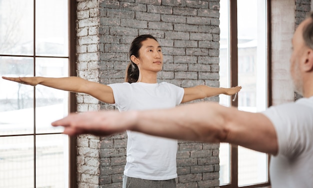 Photo attentive young brunette wearing white t-shirt holding arms in the air keeping his back straight