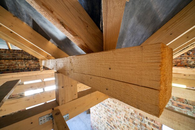 Attic of a building under construction with wooden beams of a roof structure and brick walls.