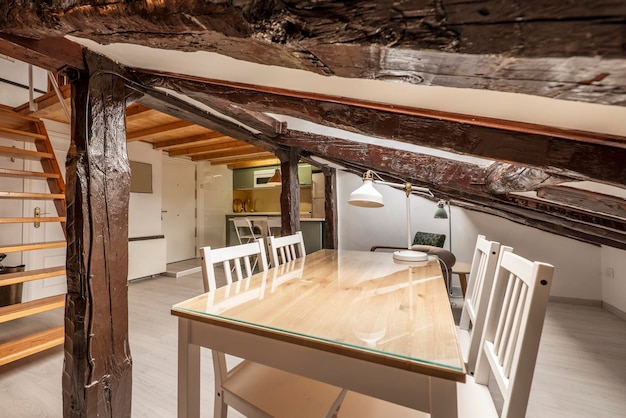 Attic room with wooden dining table and glass top white chairs and restored vintage wooden beams