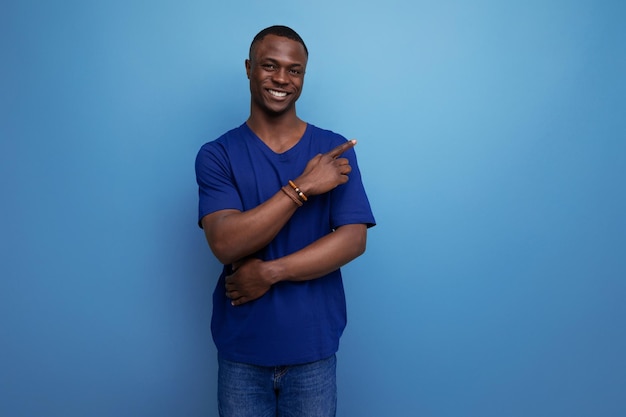 매력적인 25대 아프리카인 남자가 파란 티셔츠를 입고 손가락을 으로 가리키고 있다.