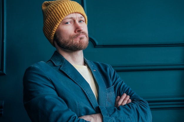 Attractive adult bearded angry man hipster in yellow hat looks at camera and furrowed brows 